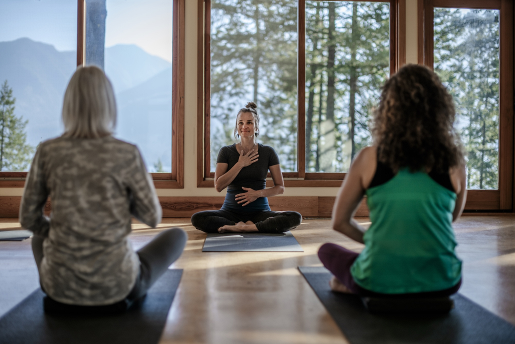 yoga instructor and students in glass front studio overlooking mountains