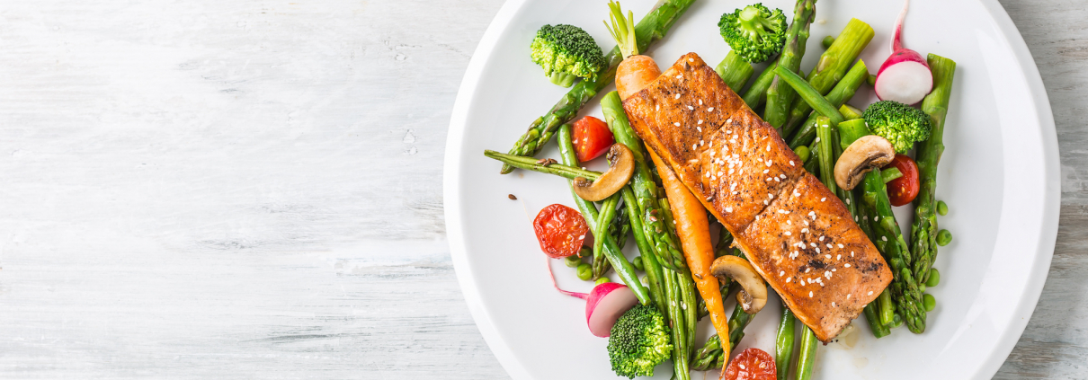 Plate with cooked salmon and veggies on blank table