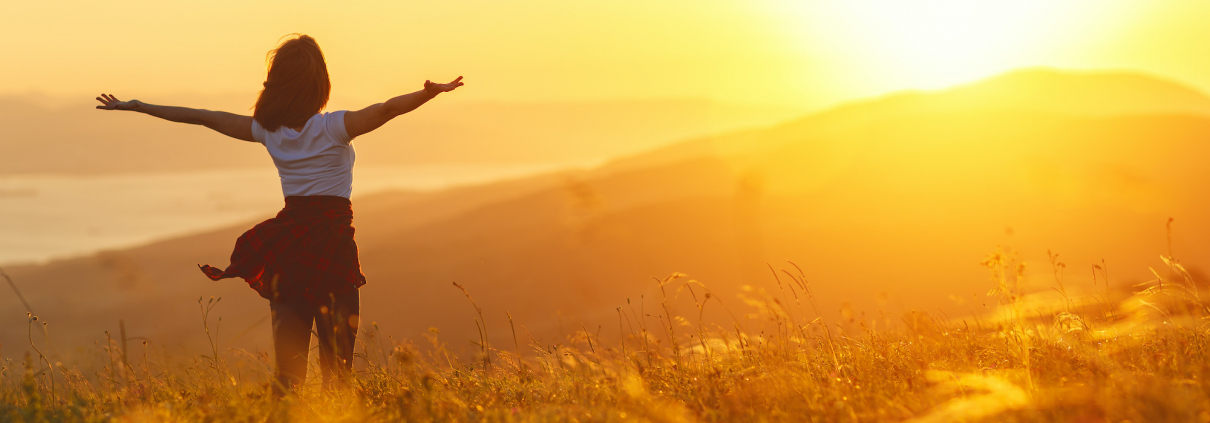 Happy woman standing with her back on the sunset in nature in summer with open hands