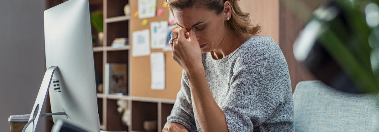 Exhausted businesswoman having a headache in modern office. Mature creative woman working at office desk with spectacles on head feeling tired. Stressed casual business woman feeling eye pain while overworking on desktop computer.