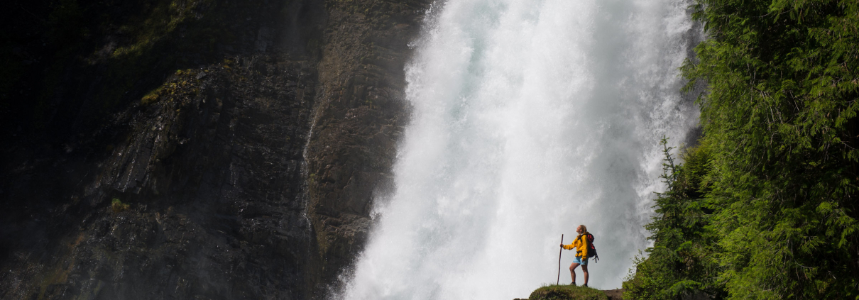 female hiker standing in front of waterfall