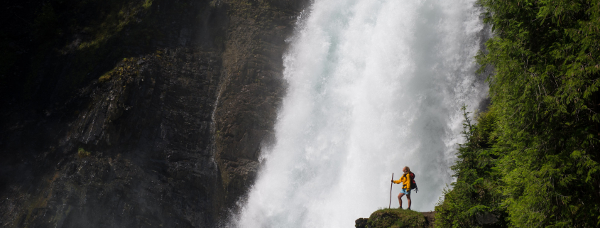 female hiker standing in front of waterfall